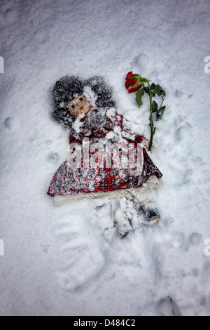 Doll enterré dans la neige avec une rose rouge Banque D'Images