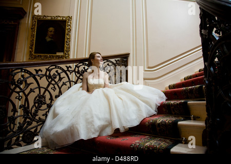 Mariée en pleine jupe robe de mariage bustier crème orné assis sur le grand escalier intérieur Banque D'Images