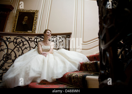 Mariée en pleine jupe robe de mariage bustier crème orné assis sur le grand escalier intérieur Banque D'Images