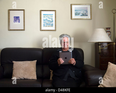 Femme mature à l'aide d'iPad à la maison assis sur le canapé Banque D'Images