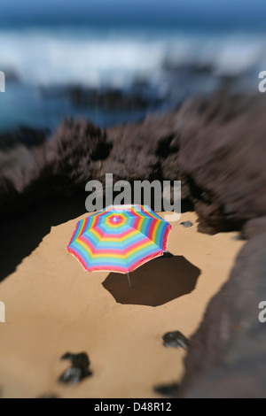 Parasol de couleur vive dans un cercle de sable entouré de pierres de lave à côté de l'océan. Banque D'Images