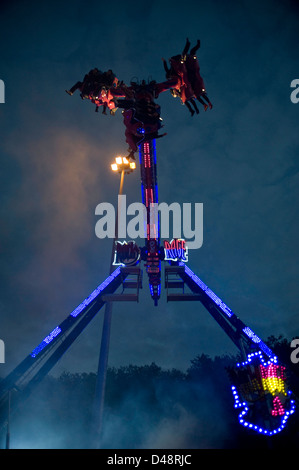 Les gens à l'envers sur un spectaculaire parc d'ride dans la soirée avec un ciel bleu en arrière-plan. Banque D'Images