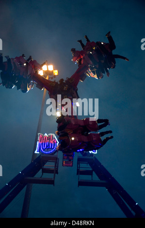 Les gens à l'envers sur un spectaculaire parc d'ride dans la soirée avec un ciel bleu en arrière-plan. Banque D'Images