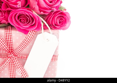 Close up d'un bouquet de roses roses à côté d'un cadeau rose avec une carte vierge sur un fond blanc Banque D'Images