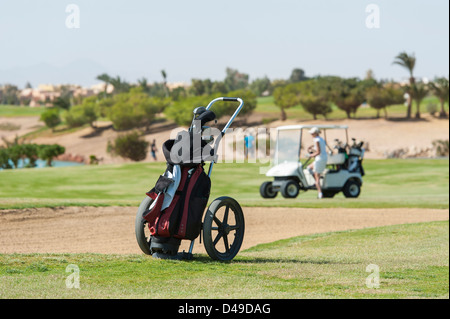 Caddy de golf trolley et sac sur le fairway avec buggy et bunker dans la distance Banque D'Images