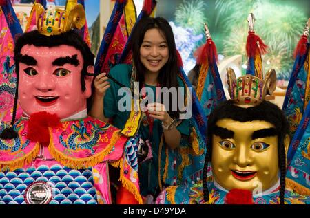 Berlin, Allemagne. 9 mars, 2013. Une jeune femme sourit comme elle se tient entre deux figures traditionnelles San Tai Zi, également connu sous le nom de "Généraux de l'Underworld' au stand de Taïwan au cours de la Foire Internationale du Tourisme (ITB, Internationalen Tourismus Börse) à Berlin, Allemagne, le 9 mars 2013. L'Indonésie est le partenaire de l'ITB en 2013. Photo : Soeren Stache/dpa/Alamy Live News Banque D'Images