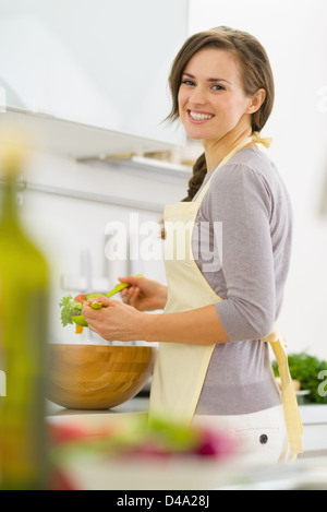 Souriante jeune femme au foyer en salade mélange cuisine moderne Banque D'Images