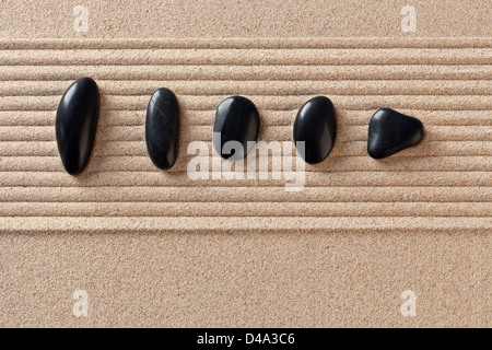 Cinq cailloux noirs sur un sable ratissée jardin zen. Banque D'Images