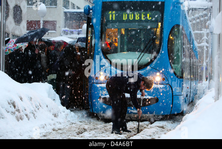 Femme pilote de tram est le nettoyage de rails pendant que les gens s'en tram dans la neige lourde. Banque D'Images