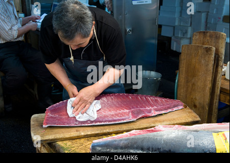 Un poissonnier met la dernière main à un grand morceau de thon frais au marché aux poissons de Tsukiji à Tokyo en gros Banque D'Images