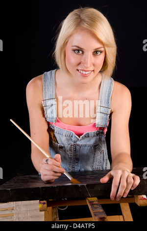 Une bonne femme blonde habillée dans des combinaisons fournit des touches de finition à la peinture de chevalet sur Banque D'Images