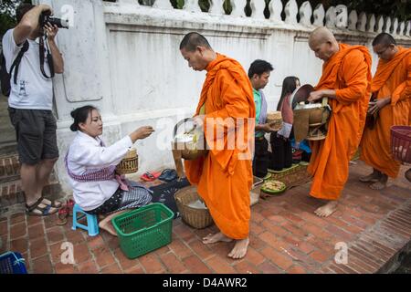 Luang Prabang, Laos. 11 mars 2013. Une des photographies touristiques des moines bouddhistes de recueillir des aumônes pendant le tak bat à Luang Prabang. Le ''Tak Bat'' est un rituel quotidien dans la plupart des du Laos (et d'autres pays bouddhiste theravada comme la Thaïlande et le Cambodge). Moines quittent leurs temples à l'aube et marche silencieusement à travers les rues et les gens mettent du riz et autres produits alimentaires dans leurs bols d'aumône. Luang Prabang, dans le nord du Laos, est particulièrement bien connu pour le matin ''tak bat'' en raison du grand nombre de temples et de moines dans la ville Crédit : ZUMA Press, Inc. / Alamy Live News Banque D'Images
