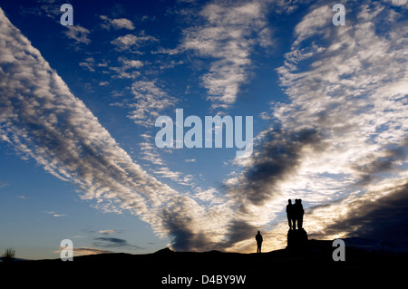 Une personne silhouettée contre un lever de soleil spectaculaire cloudscape et le Mémorial Commando à Spean Bridge dans les Highlands écossais Banque D'Images