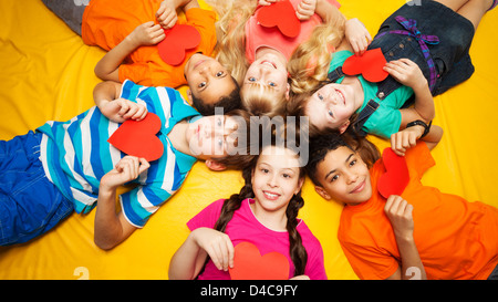 Groupe d'enfants heureux pose en cercle sur le sol avec des coeurs dans leurs mains Banque D'Images