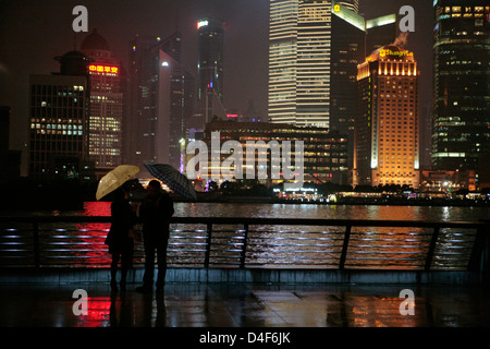 Une nuit pluvieuse dans le Bund de Shanghai, deux touristes à l'abri sous les parasols en regardant l'allumé Pudong District. Banque D'Images