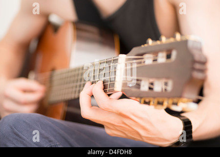 Les jeunes adultes de sexe masculin se détendre et jouer sur sa guitare acoustique Banque D'Images