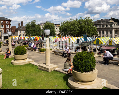 Les auvents de couleur vive sur le marché de fourniture de Norwich avec des gens assis à l'avant-plan de la zone de pavage et de l'espace herbeux Banque D'Images