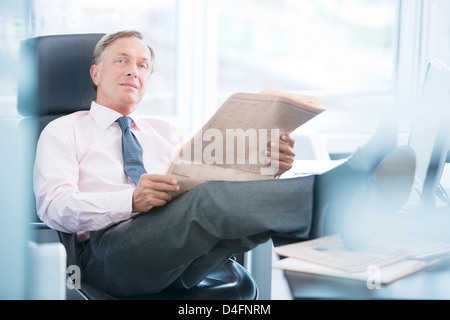 Businessman reading newspaper in office Banque D'Images