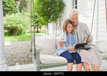 Petite-fille et femme lecture le porche swing Banque D'Images