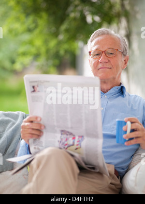 Man reading newspaper in porch swing Banque D'Images