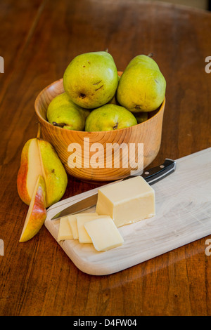 Un bol de poires Bartlett fraîches sur une table en bois avec des tranches de fromage et un couteau d'office sur une planche à découper en bois et d'une poire coupée Banque D'Images