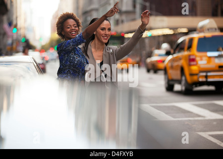 Women hailing taxi on city street Banque D'Images