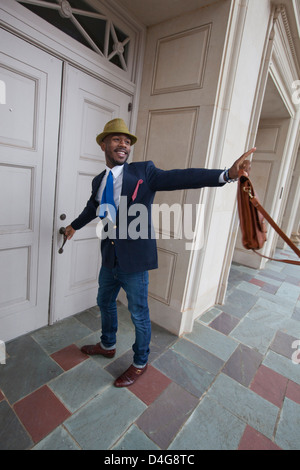 Un quartier chic young African American man looking back et agitant un accueil sympa comme il l'est l'ouverture d'une porte. Banque D'Images