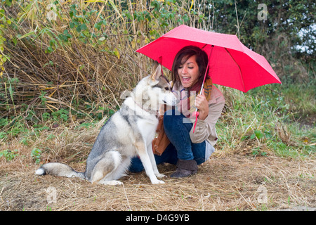 Adolescente avec chien malamute d'Alaska à l'abri de la pluie sous parapluie rouge sur un pays à pied Banque D'Images