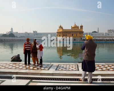Un temple garde au Temple d'or d'Amritsar avec Punjabi famille devant la sainte piscine sous un ciel bleu Banque D'Images