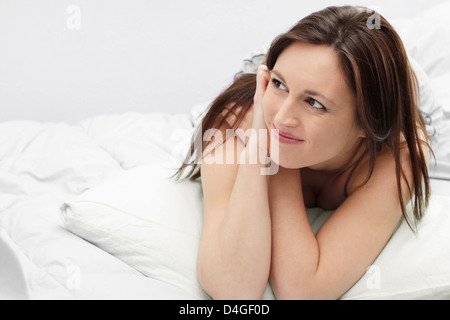 Jeune femme dans la fin des années 20 - début des années 30, reposant et smiling on bed.White doublures et la structure horizontale Banque D'Images