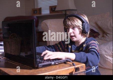 Jeune garçon blanc dans un salon regardant un écran d'ordinateur portable avec casque pour se concentrer sur le verrouillage de l'école à domicile ou jouer à un jeu sur ordinateur Banque D'Images