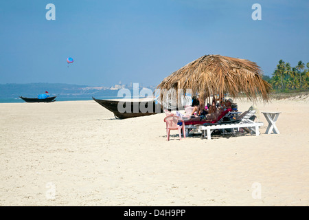 Les vacanciers au soleil à l'ombre des parasols de la noix de coco. Le sable blanc, ciel bleu, mer, surf et pêche bateaux locaux Banque D'Images