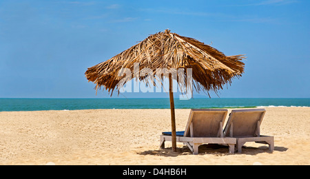 Plage déserte tropicale avec chaises longues sous un parasol de feuilles de coco. Ciel bleu, océan, surf douce et propre plage de sable. Banque D'Images