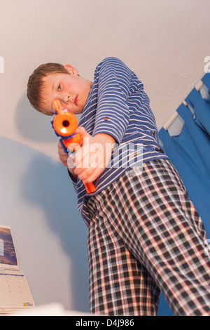 Un garçon de neuf ans avec un pistolet nerf dans sa chambre à coucher Banque D'Images