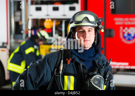 Jeune pompier en uniforme debout devant des pompiers, il est prêt pour le déploiement Banque D'Images