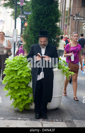 Un représentant juif lisant un livre dans la rue à New York, USA Banque D'Images