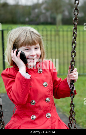 8 ans girl laughing et talking on mobile phone alors que dire sur swing. Banque D'Images