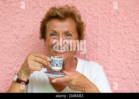 Dame plus âgée de boire son café turc en face du mur texturé rose Banque D'Images