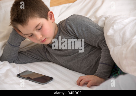 Huit ans kid regardant montre sur Daddy's smart phone avant qu'il se met en veille. Banque D'Images