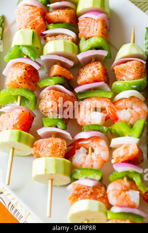 Cubes de saumon et de crevettes a complimenté avec légumes sur les brochettes. Prêt à cuire. Oignons rouges, courgettes et poivrons verts. Banque D'Images