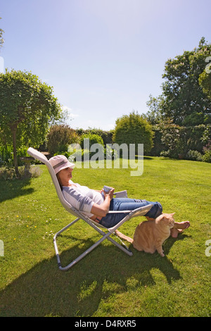 Mature Woman Sitting in Deckchair et relaxant dans jardin sur une journée de printemps ensoleillée Banque D'Images
