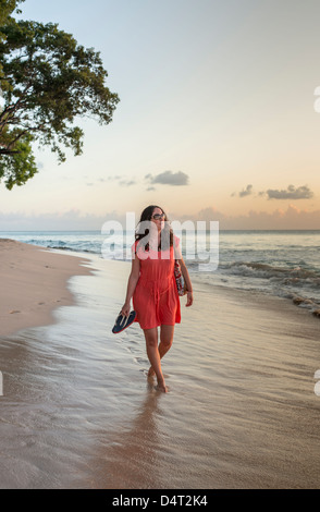 Une femme marche le long de la plage au coucher du soleil, près de Holetown, paroisse de Saint James, Barbade Banque D'Images