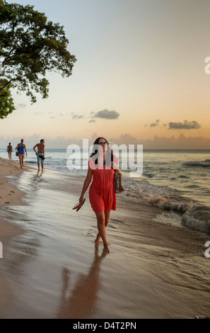 Une femme marche le long de la plage au coucher du soleil, près de Holetown, paroisse de Saint James, Barbade Banque D'Images