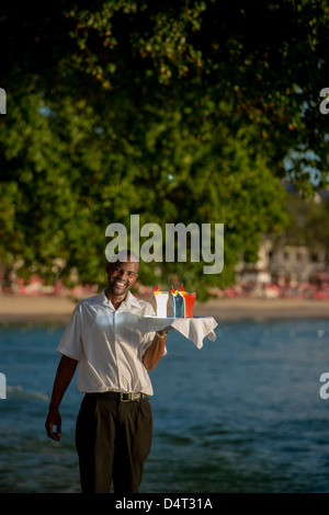 Un waiter holding un bac de cocktails sur la côte ouest de la Barbade, Holetown (Sandy Lane en arrière-plan) Banque D'Images