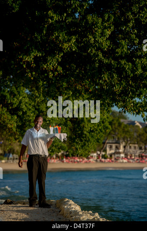 Un waiter holding un bac de cocktails sur la côte ouest de la Barbade, Holetown (Sandy Lane en arrière-plan) Banque D'Images