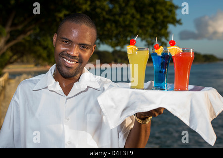 Un waiter holding un bac de cocktails sur la côte ouest de la Barbade, Holetown (Sandy Lane en arrière-plan) Banque D'Images