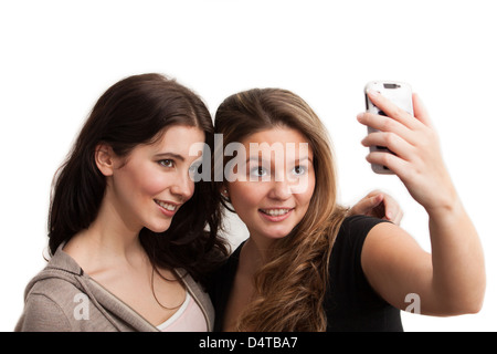 Deux jeunes femmes à la recherche sur leur téléphone intelligent prendre une photo d'eux-mêmes. Isolé sur fond blanc Banque D'Images