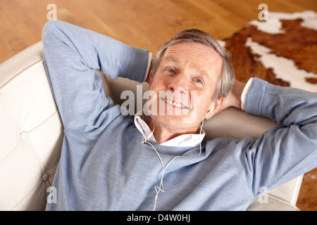 Older Man listening to earphones on sofa Banque D'Images