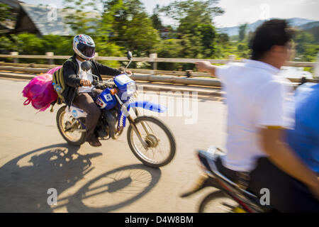 12 mars 2013 - Oudomxay, d'Oudomxay, Laos - Motos sur l'autoroute 13 utiliser le pont sur la rivière Nam Kor dans Oudomaxy. L'asphaltage de l'autoroute 13 de Vientiane à près de la frontière chinoise a changé le mode de vie dans les régions rurales du Laos. Les villageois près de Luang Prabang l'habitude d'avoir à prendre des bateaux peu fiable qui a duré trois heures aller-retour pour se rendre de la maison au centre touristique de Luang Prabang, maintenant ils prennent un aller-retour de 40 minutes en bus. Au nord de Luang Prabang, ouvrant ainsi la voie publique a été l'occasion pour la Chine d'utiliser le Laos en tant que point de transbordement. Marchandises chinois passe maintenant par le Laos à Banque D'Images