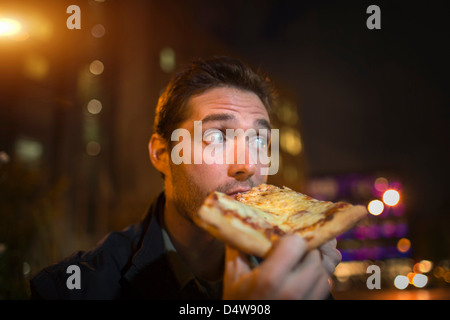 Man eating pizza on city street Banque D'Images